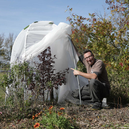 Gardener points to plants inside a white fabric frost protection cover. Essential for winterizing delicate garden plants.