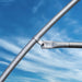 Galvanized steel pipe fitting with clamp and bolt for structural support against a sunny blue sky.