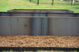 Weathered steel raised garden beds with brown gravel on a green lawn, black fence in the background.