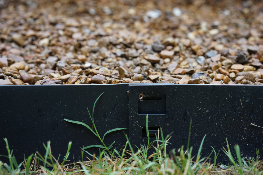 Black landscape edging cleanly separates green grass from a gravel path, featuring an interlocking connection.