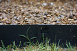 Black landscape edging cleanly separates green grass from a gravel path, featuring an interlocking connection.