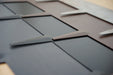 Industrial metal sheet with overlapping dark grey and bronze geometric cutouts, modern design.