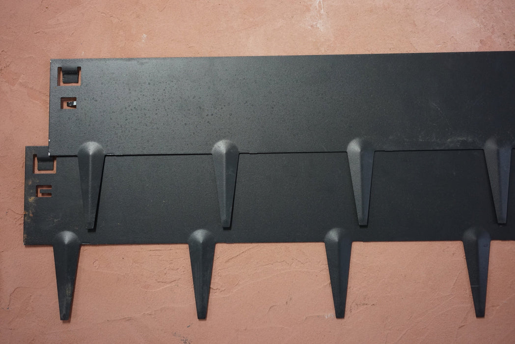Modern black wall-mounted coat rack with six hooks on a textured terracotta wall. Entryway organization.