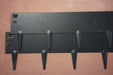 Modern black wall-mounted coat rack with six hooks on a textured terracotta wall. Entryway organization.