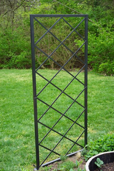 Black metal garden trellis featuring a diagonal grid design, ideal for climbing plants in a lush backyard.