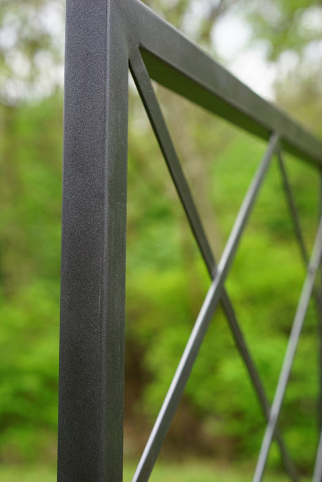 Textured black metal fence post and lattice design with blurred green foliage. Modern outdoor garden fencing.