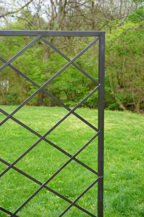 Black metal garden trellis with diamond lattice pattern against a green lawn and trees.