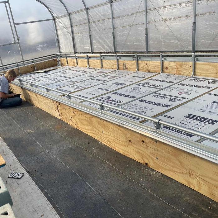 Woman installing R-Matte foam insulation in a plywood raised bed within a greenhouse for season extension.