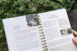 Gardening journal open to seed selection & storage tips. Pages titled "Shop for Seeds" & "Organize Old Seeds." Green plant background.