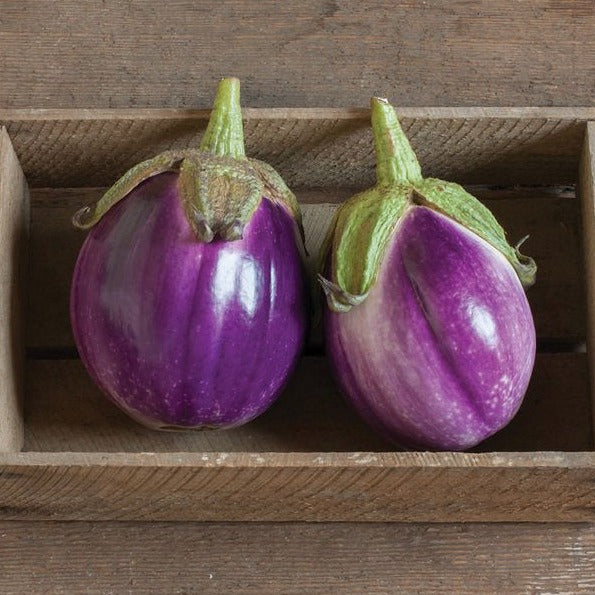 Two fresh purple eggplants with green caps in a wooden crate.