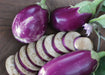 Fresh purple eggplants, whole and sliced, on wood. One mottled, another with a small purple flower.