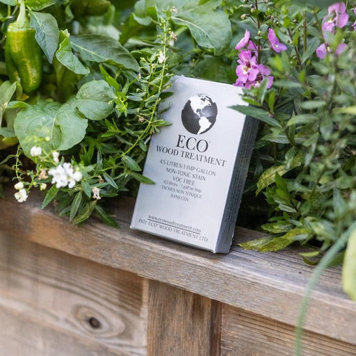 ECO Wood Treatment non-toxic, VOC-free wood stain box on a wooden surface with lush garden plants and flowers.