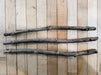 Three weathered tree branches with rough bark on a light brown wood plank background. Rustic, natural texture.