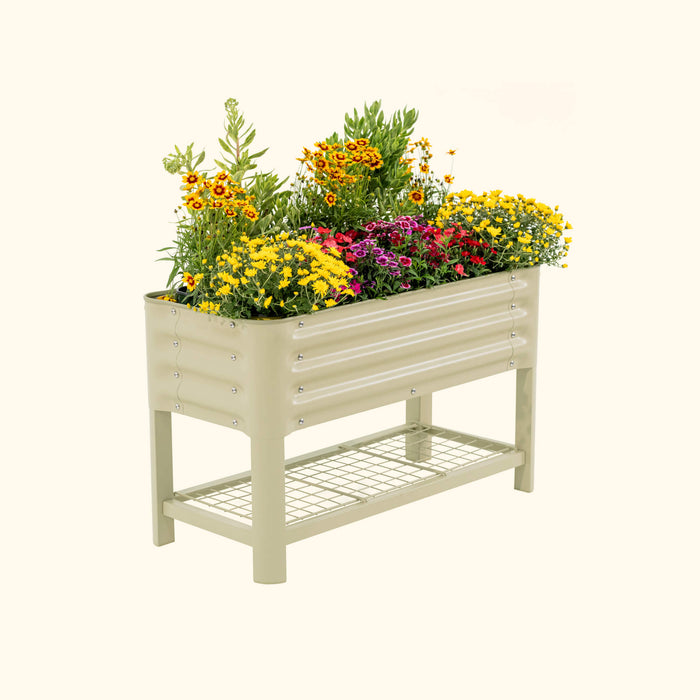 Sage green metal raised garden bed with colorful yellow, red, and purple flowers. Elevated planter box with storage shelf.