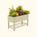 Sage green metal raised garden bed with colorful yellow, red, and purple flowers. Elevated planter box with storage shelf.