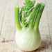 Fresh fennel bulb with vibrant green fronds and stalks on a light wooden background.