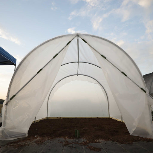Open hoop house greenhouse with translucent cover, metal frame, and rich dark soil ready for planting.