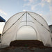 Open hoop house greenhouse with translucent cover, metal frame, and rich dark soil ready for planting.