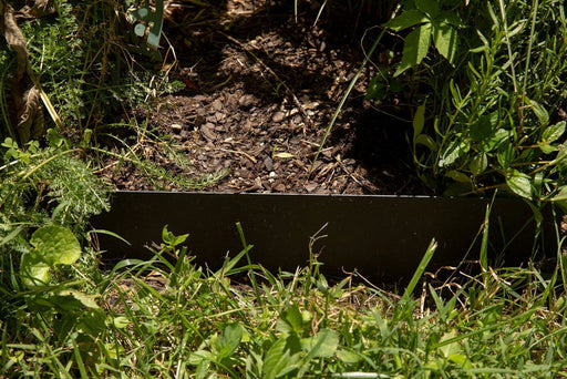 Metal landscape edging separating lush green grass from a mulched garden bed with various plants and herbs.