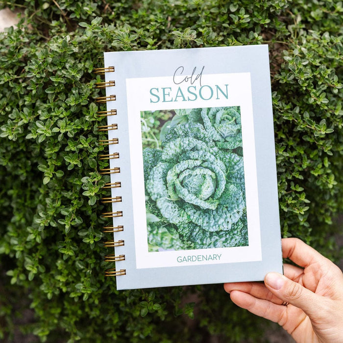 Hand holds "Cold SEASON" Gardenary planner with a vibrant savoy cabbage cover, perfect for winter garden planning.