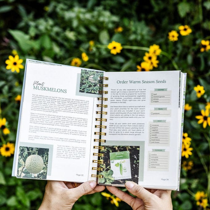 Hands hold a spiral-bound gardening planner showing muskmelon planting tips and warm season seed order list, with yellow flowers.