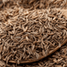 Whole cumin seeds on a wooden spoon, a popular spice for cooking and seasoning.