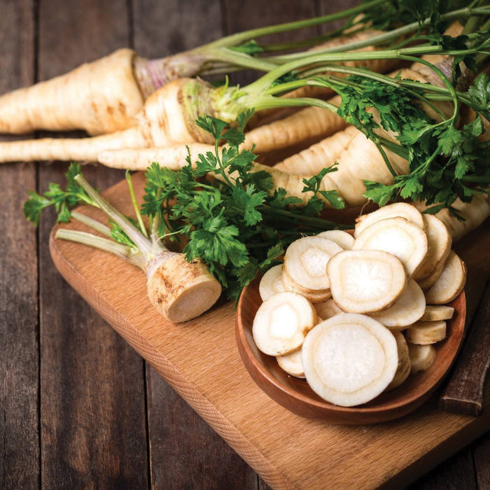 Fresh whole and sliced parsnips with green tops on a rustic wooden board. Healthy root vegetables.