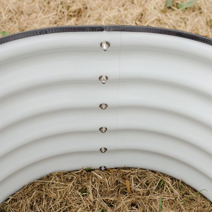 White corrugated metal raised garden bed with black safety trim, visible bolts, and straw mulch inside, showing sprouts.