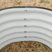 White corrugated metal raised garden bed with black safety trim, visible bolts, and straw mulch inside, showing sprouts.