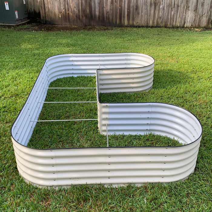 Outdoor L-shaped light grey corrugated steel raised garden bed with internal support rods on green grass.