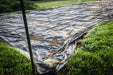 Black plastic weed control tarp covering a garden bed, surrounded by dew-kissed green grass.