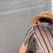 Person's back in a straw hat and grey striped shirt. Light grey background with subtle texture.