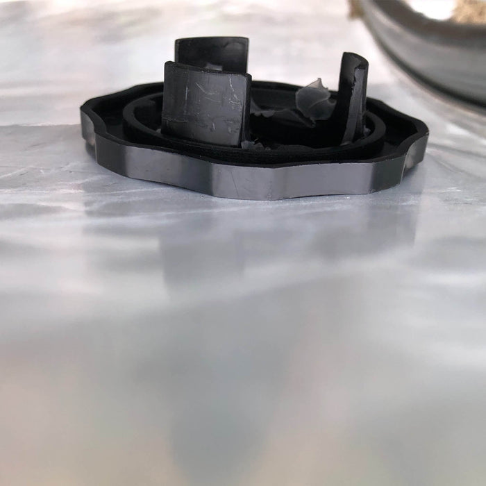 Damaged black blender drive coupling with broken fins, replacement part on a light surface.