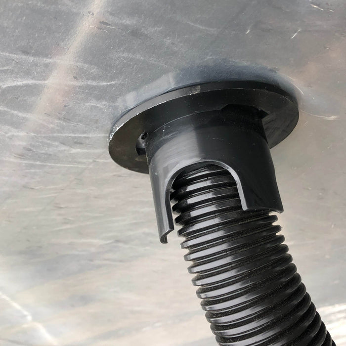 Black corrugated hose connected to a plastic bulkhead fitting on a grey surface. Drainage or electrical conduit.
