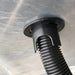 Black corrugated hose connected to a plastic bulkhead fitting on a grey surface. Drainage or electrical conduit.