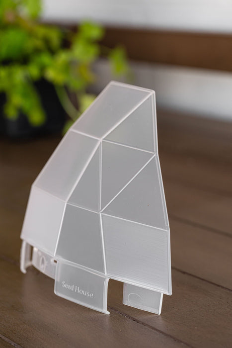 Translucent geometric "Seed House" seed starter cover on a wooden surface for plant germination.