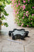 Durable black plastic rolling plant caddy on a stone patio, next to a strawberry tower and vibrant pink petunias.