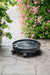 Black rolling plant caddy with drainage tube on patio pavers, next to potted strawberries and pink petunias.