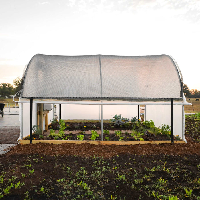 Shade net hoop house protecting raised garden beds with growing organic vegetables: lettuce, kale, and greens.