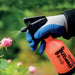 Blue-gloved hand sprays pink rose with orange 0.5L Super Mercury garden sprayer for plant care.