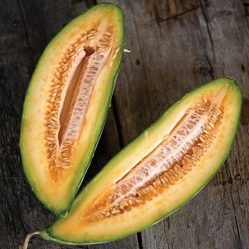 Oblong melon cut in half, revealing green rind, orange-yellow flesh, and seeds on wood. Fresh, healthy fruit.