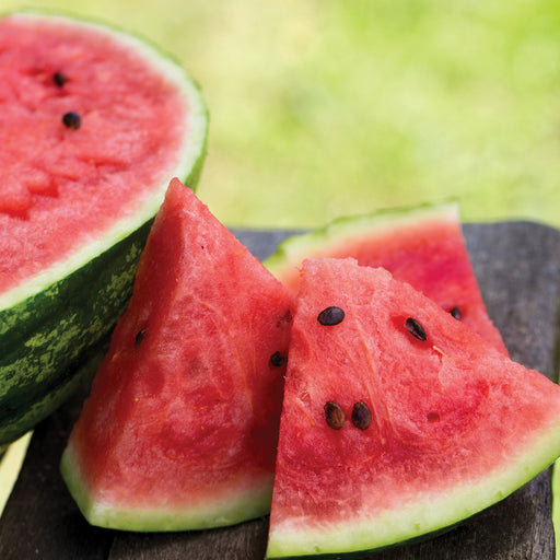 Fresh, vibrant red watermelon slices and a half melon with seeds on a rustic wooden table. Perfect summer fruit.