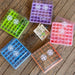Colorful seed starter trays with clear vented lids, some with soil & seedlings. Seed packet, trowel. Home gardening.