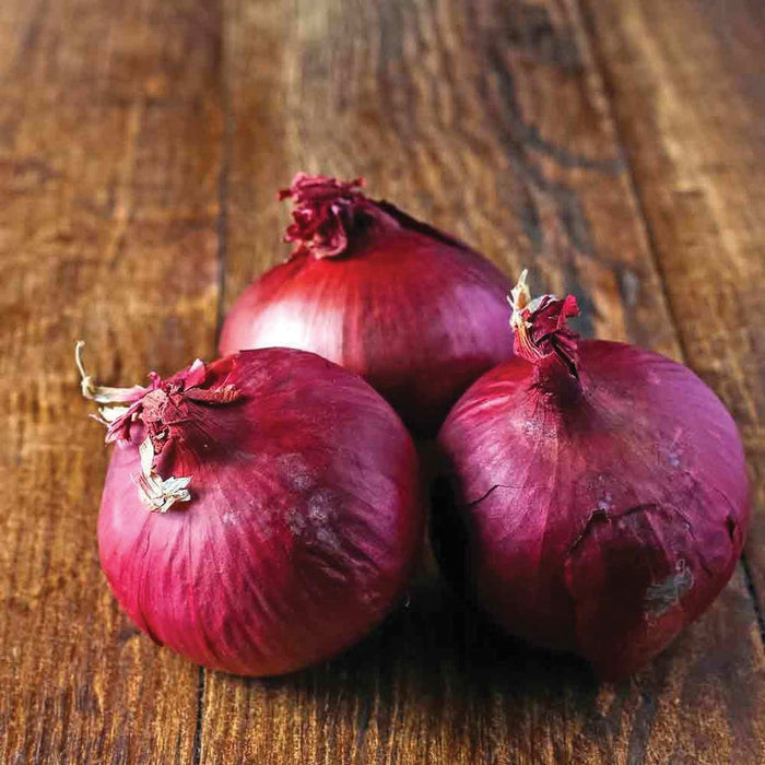 Three fresh red onions on a rustic wooden table.