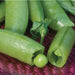 Fresh green pea pods, one split open with a single pea, others full of garden peas, on a textured red surface.