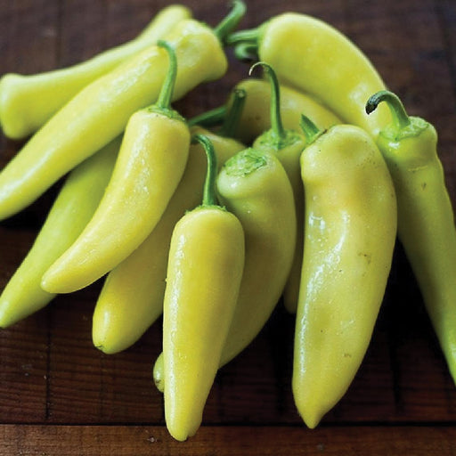 Fresh pale yellow banana peppers on a rustic wooden surface. Mild chili peppers for cooking and pickling.