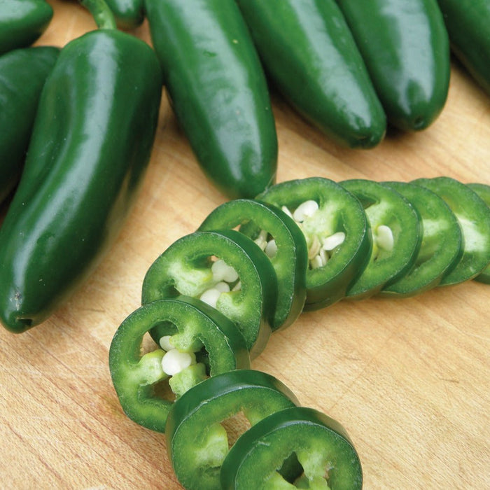 Fresh green jalapeños, whole and sliced, on a wooden cutting board. Spicy chili peppers for cooking.