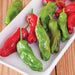 Bright green and red shishito peppers on a white platter. Fresh, colorful produce for cooking.