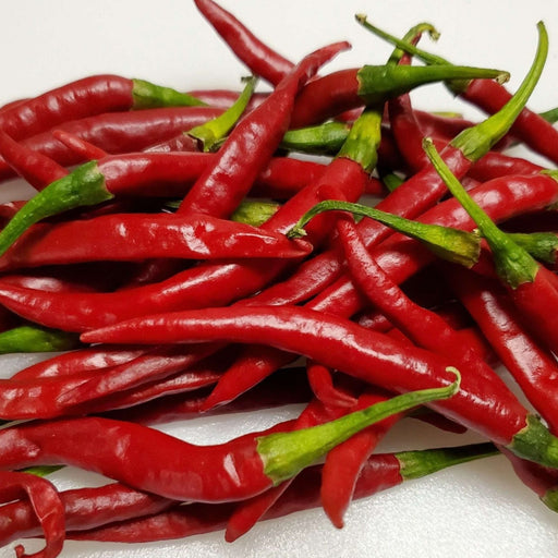Pile of vibrant red chili peppers with green stems on a white background. Fresh, spicy cooking ingredient.
