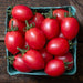 Ripe red grape tomatoes with green stems in a blue carton. Fresh, healthy produce on rustic wood.